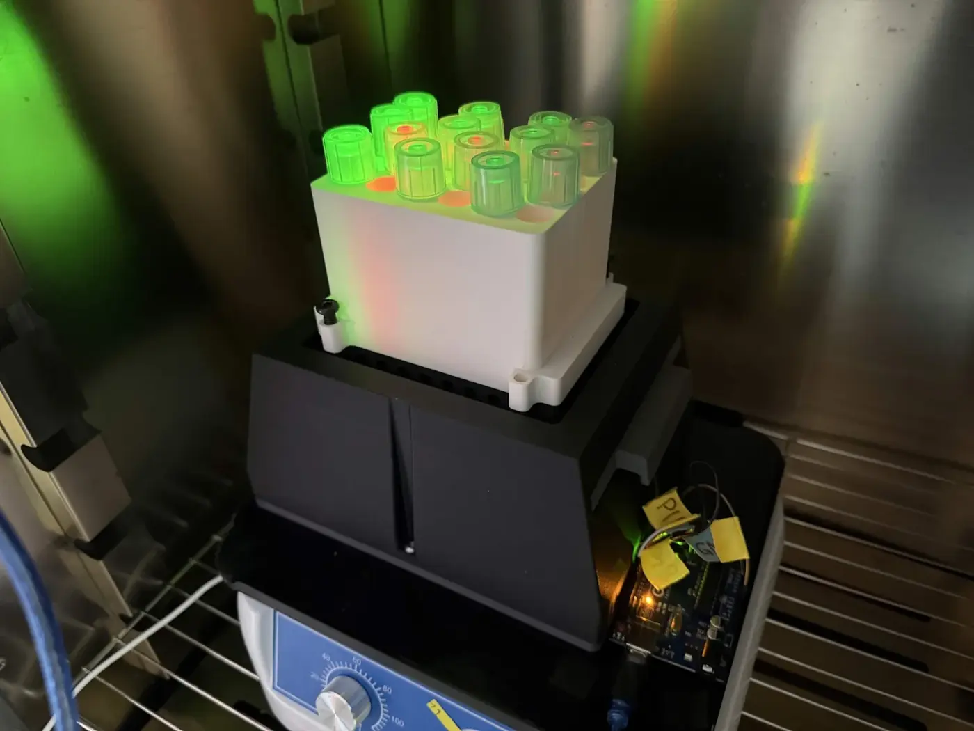 LPA in an incubator: a tube holder of culture tubes glowing green under its LEDs, on a shaker.