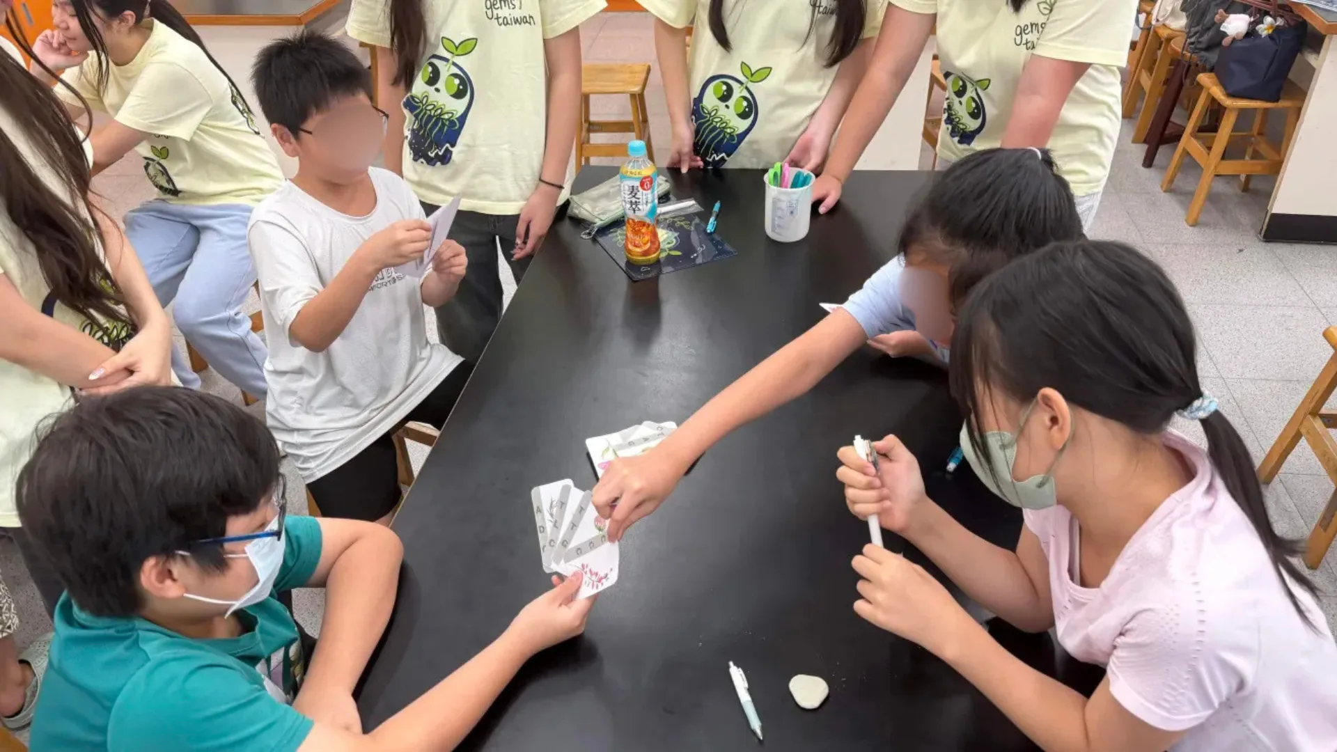 Elementary students leaning over a lab bench, holding and matching ATCG cards.