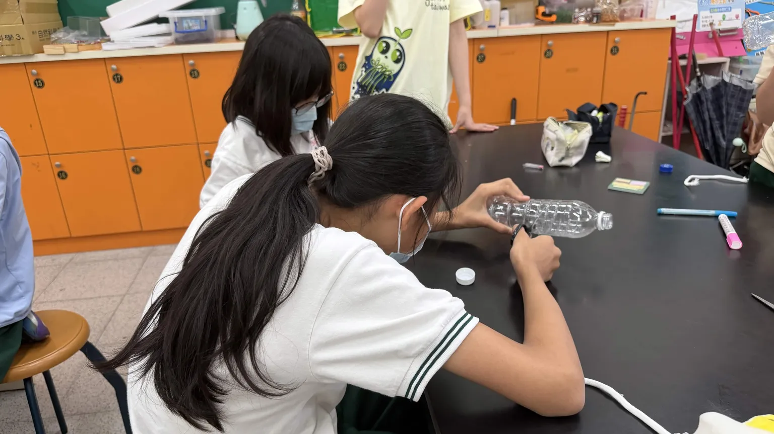 A student cutting and assembling a plastic bottle into a self-watering planter at a lab bench.