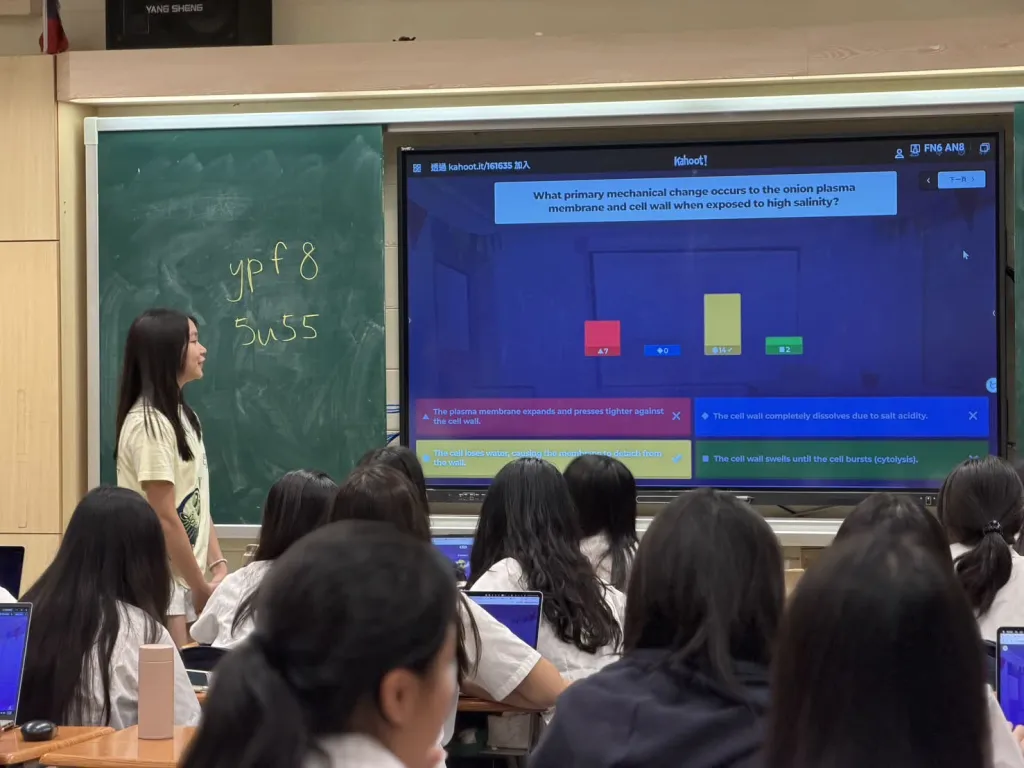 A team member beside a screen showing a Kahoot question, with high school students seated in front.