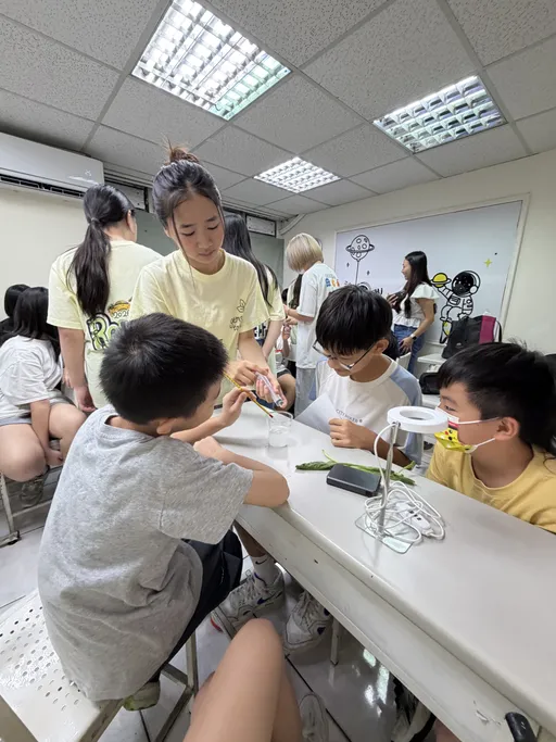 Junior high students at a table with beakers and worksheets during the leaf-disk experiment, a team member standing behind them.