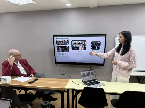 A student presenting on a wall screen to a man seated at a table.