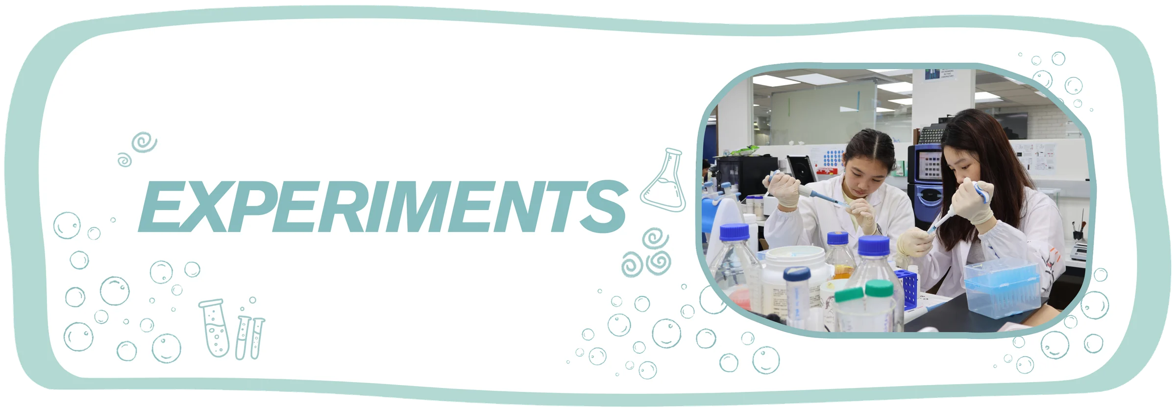 Experiments. Two team members in white coats and gloves pipette at a bench crowded with media bottles.