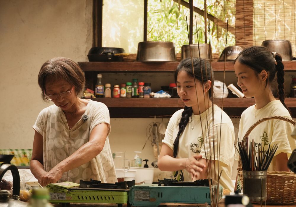 Farmer Chen cooking at a camp stove as two ReLEAF students watch beside her.