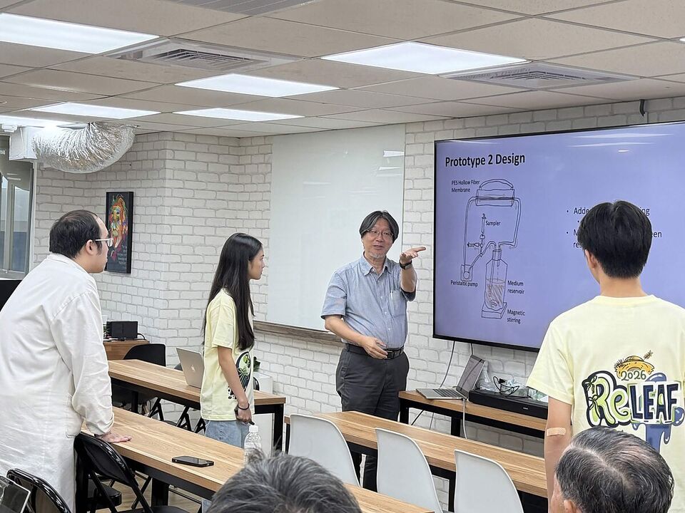 Prof. Chang points to a &ldquo;Prototype 2 Design&rdquo; bioreactor slide while ReLEAF students in team shirts listen.