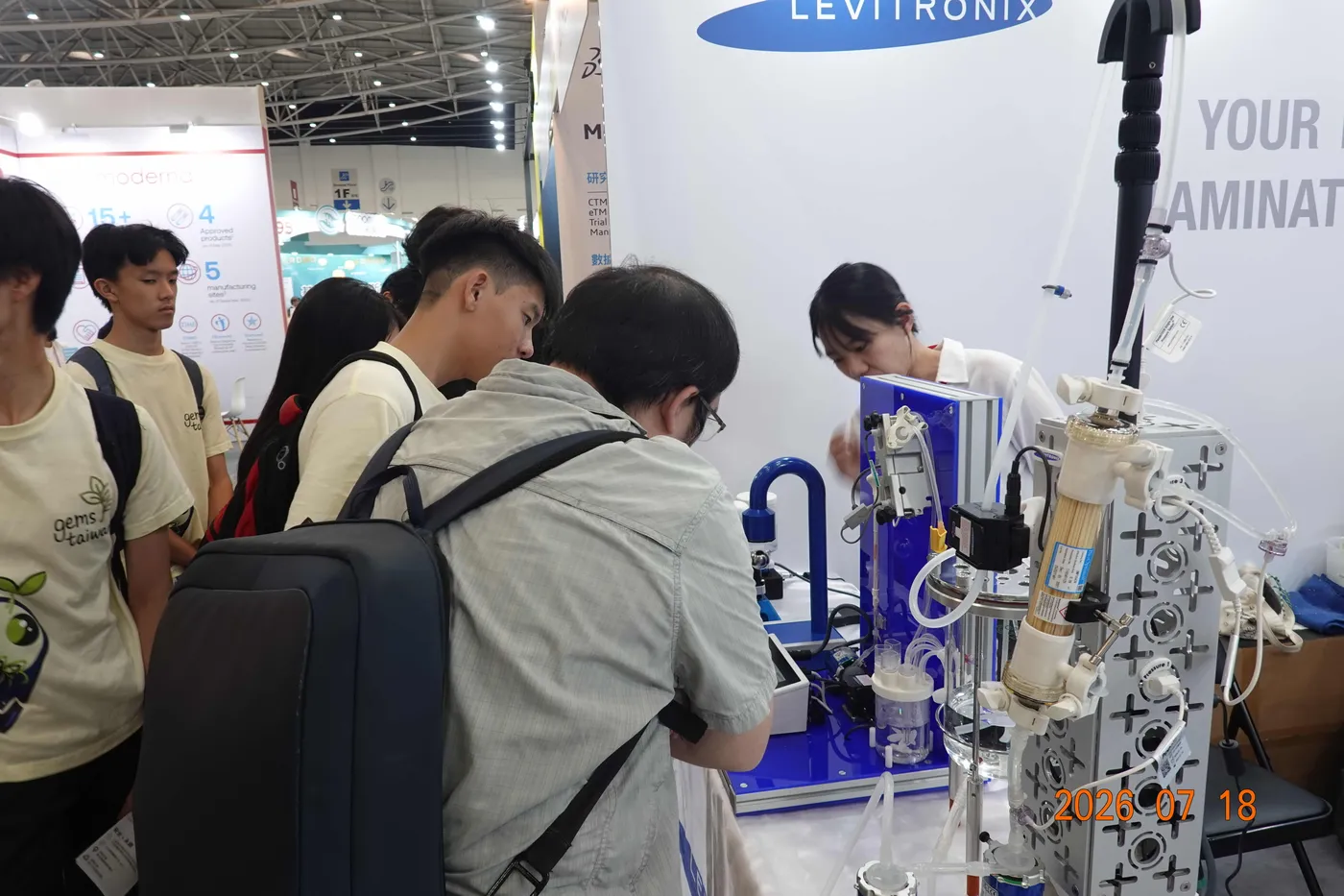Students crowded around a hollow-fibre filtration rig at a trade exhibition booth while a company representative demonstrates it.
