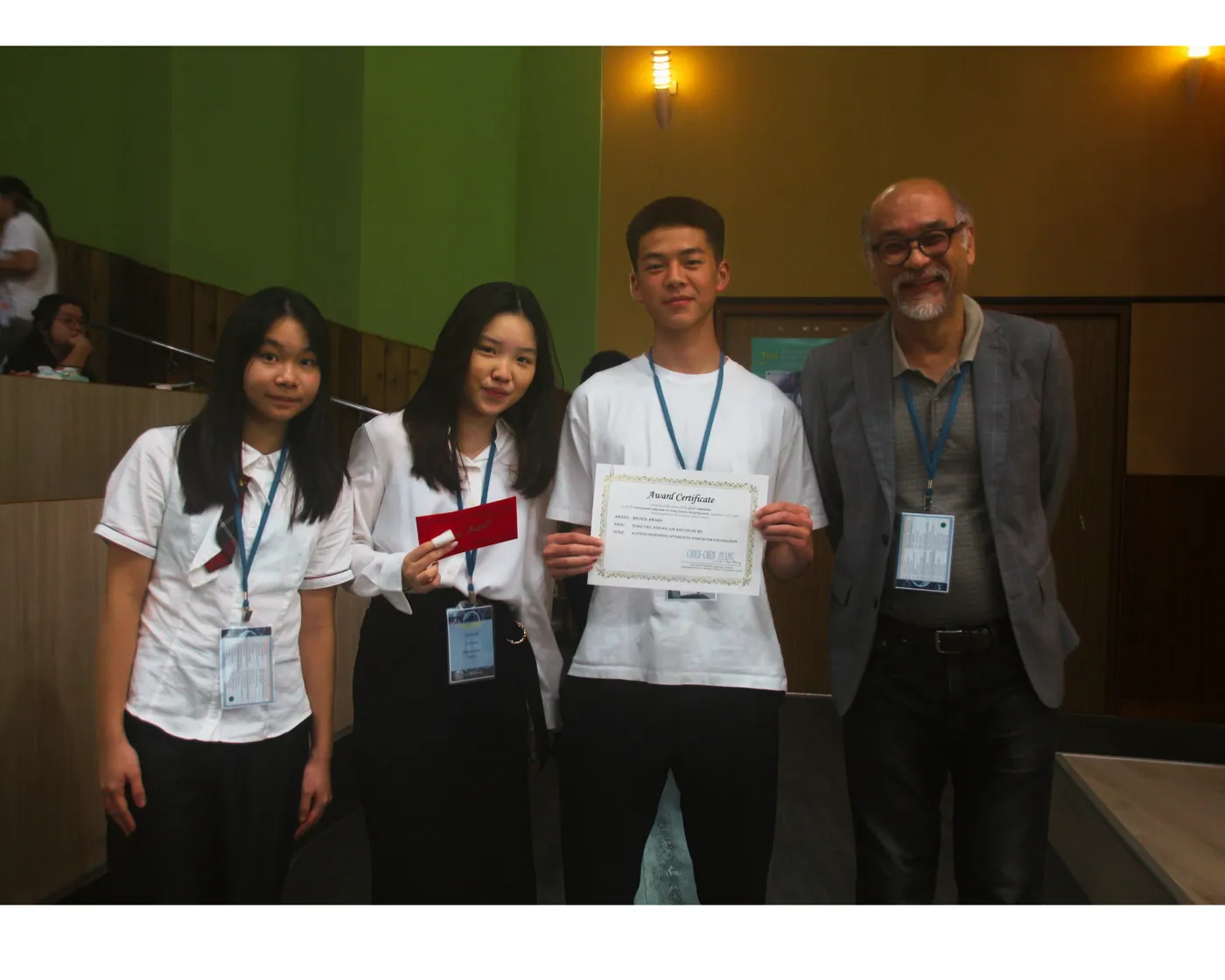 Three students holding a certificate beside Prof. Huang.