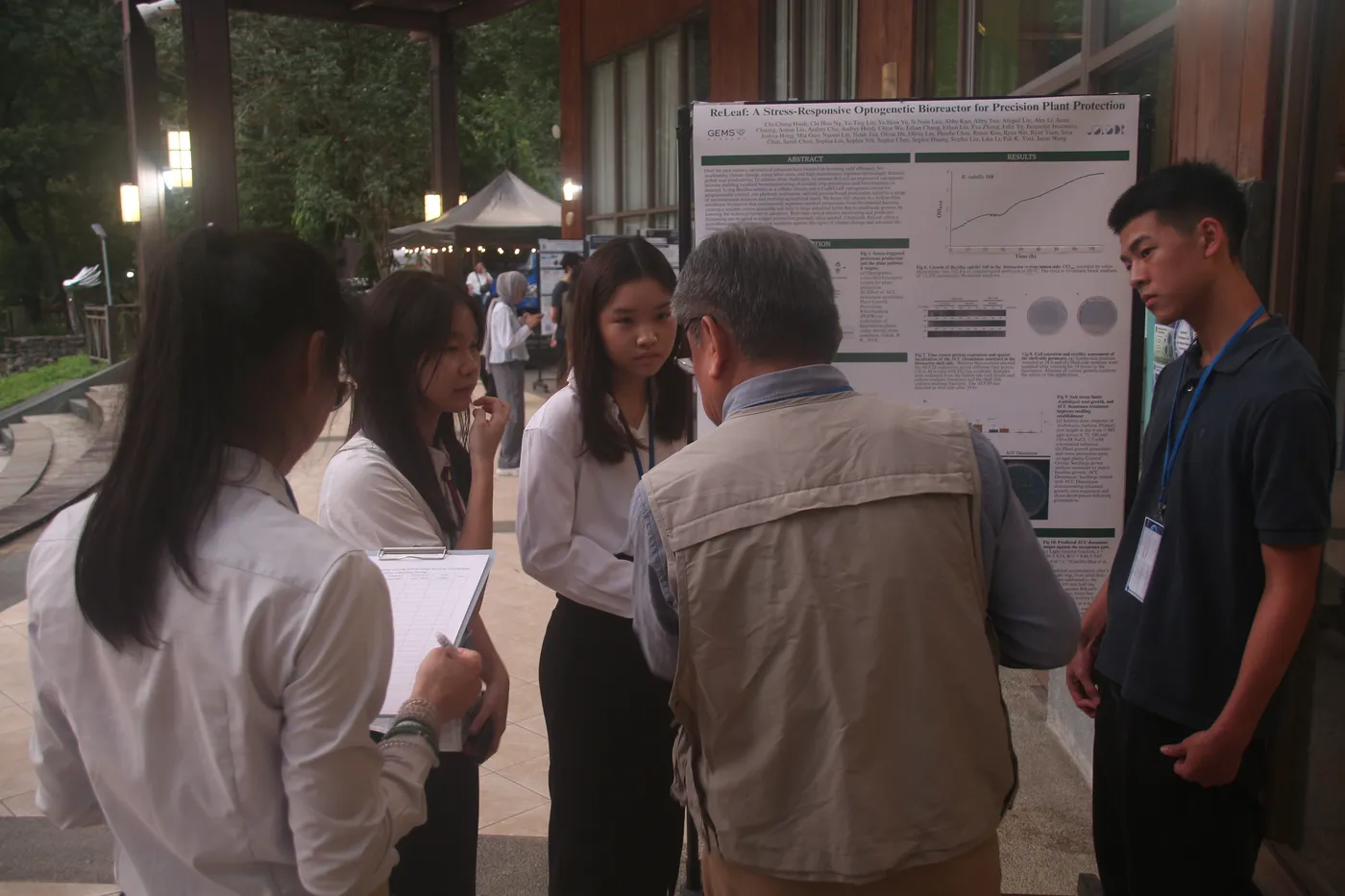Students explaining the poster to an older visitor at an evening poster session.
