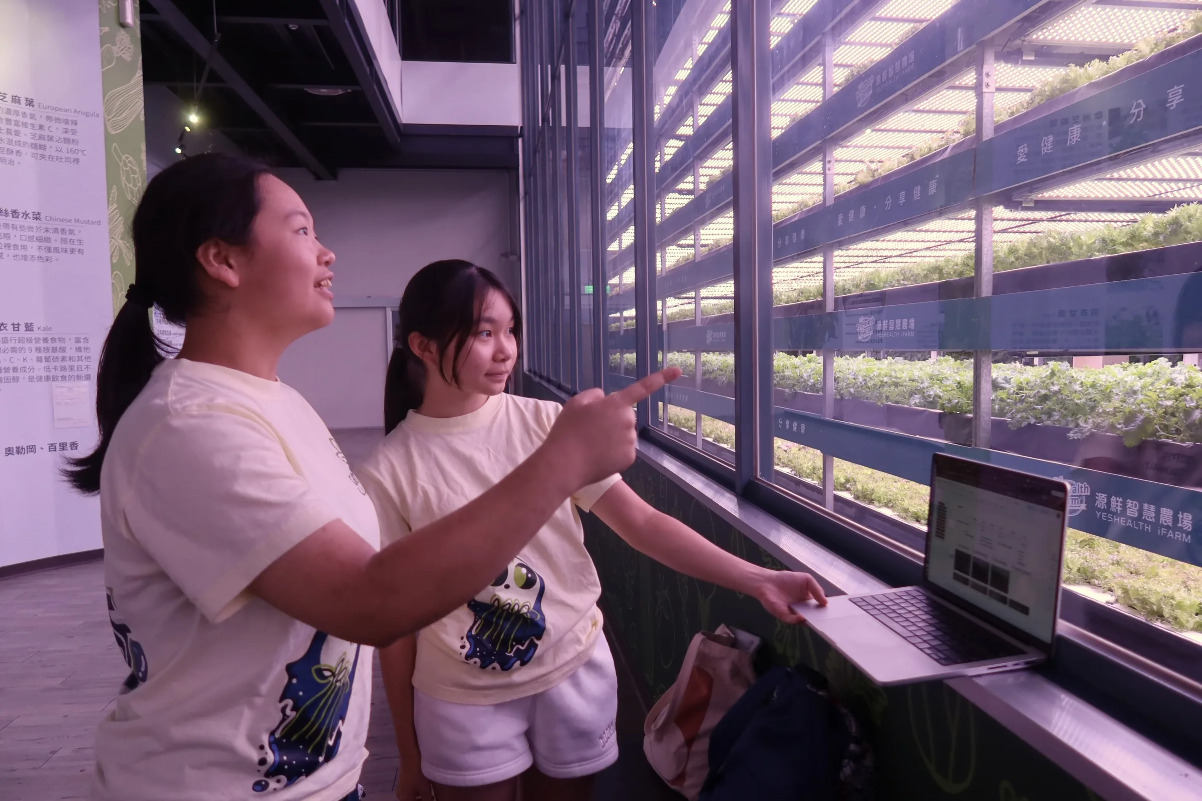 Two students beside the lit growing racks, one pointing at the shelves.