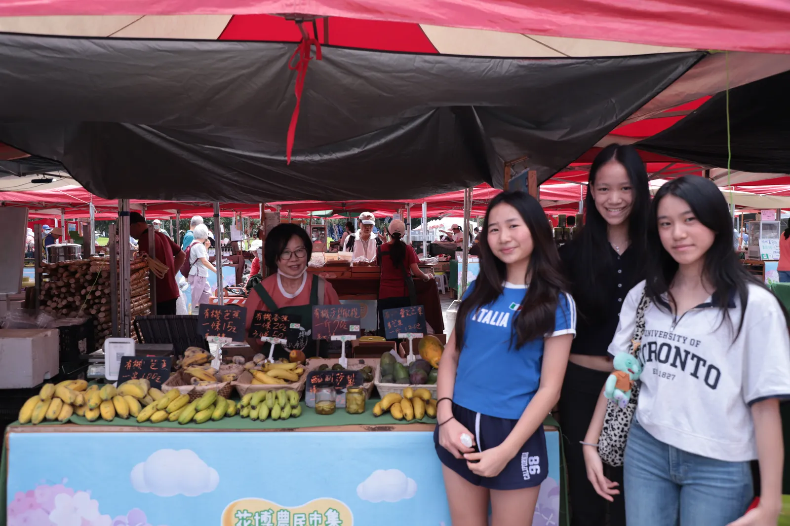Four students smiling at a market stall under a red tent.