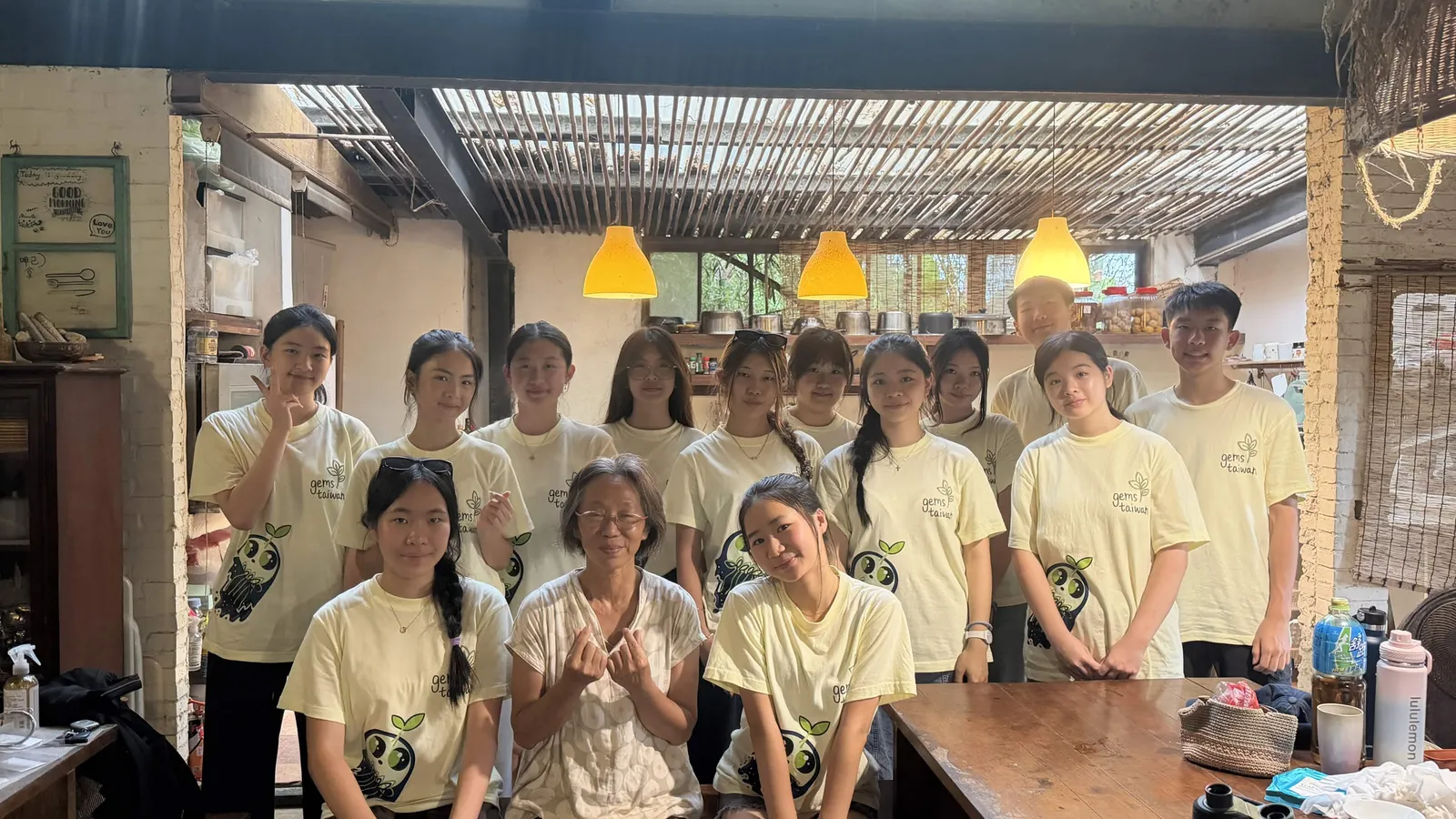 The team, a teacher and Ms. Chen in her kitchen, some making peace signs.