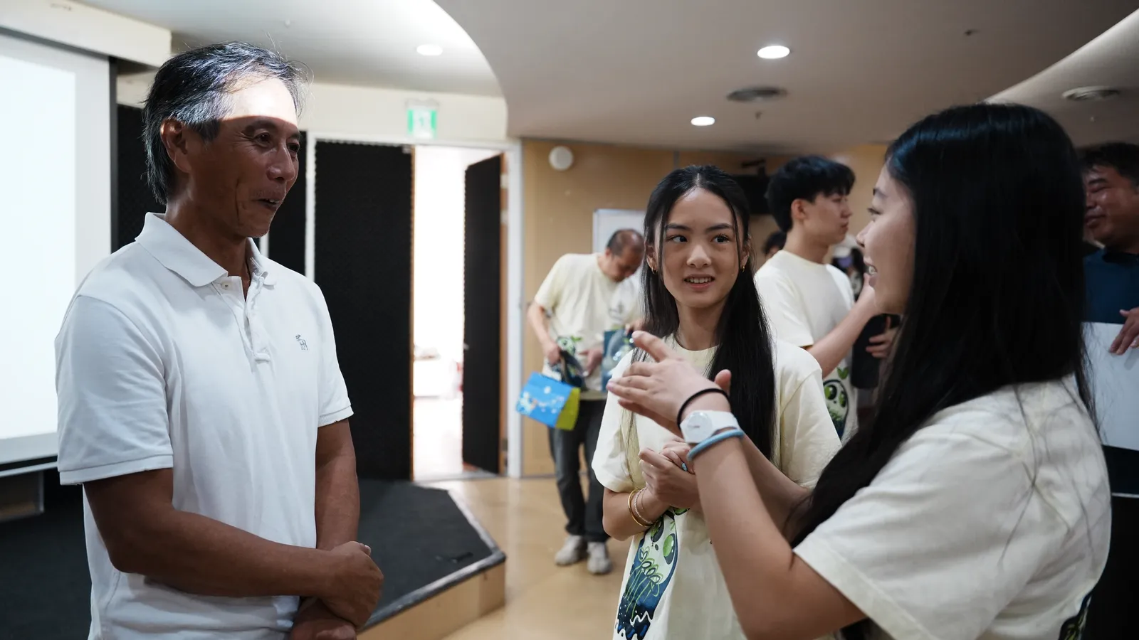 Two students talking with a man in a white shirt and cap.