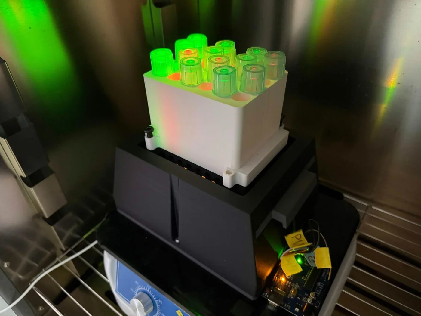 The light plate apparatus loaded with culture tubes glowing green inside an incubator.