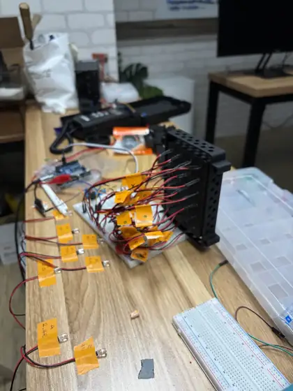 Individual LEDs taped down in rows across a bench with handwritten labels, beside the black light-plate housing wired up with red and black leads and a breadboard.