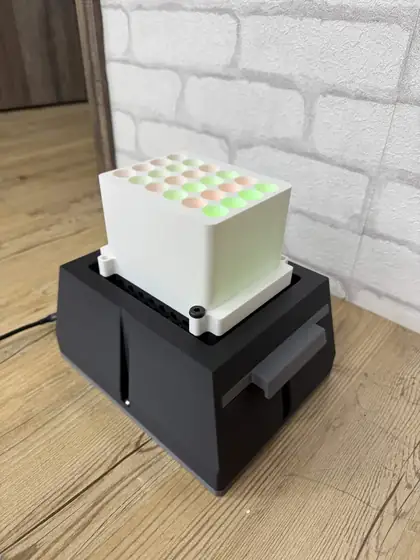 The assembled light plate apparatus: a black 3D-printed base with a white well plate on top, its grid of wells glowing alternately amber and green.