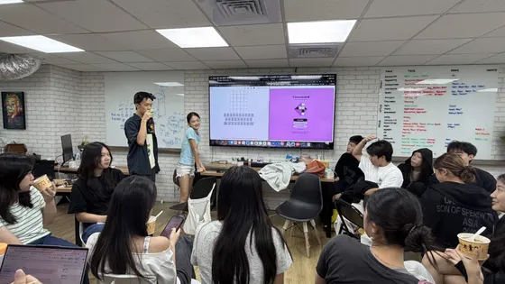 A student standing at the screen talking to the rest of the team, everyone turned towards the front of the room.