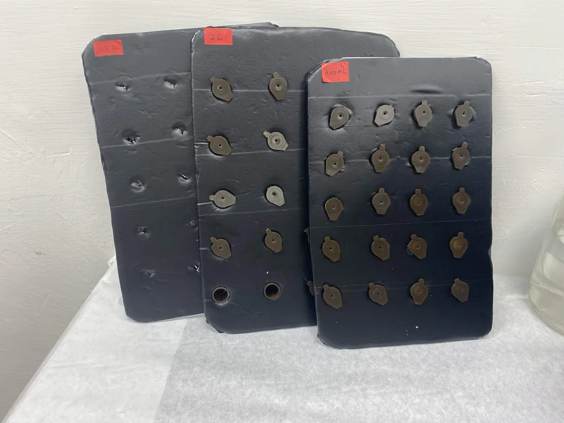 Three black perforated foam boards leaning against a wall on a bench, hand-labelled in red tape with 1.5 L, 2 L and 300 mL.