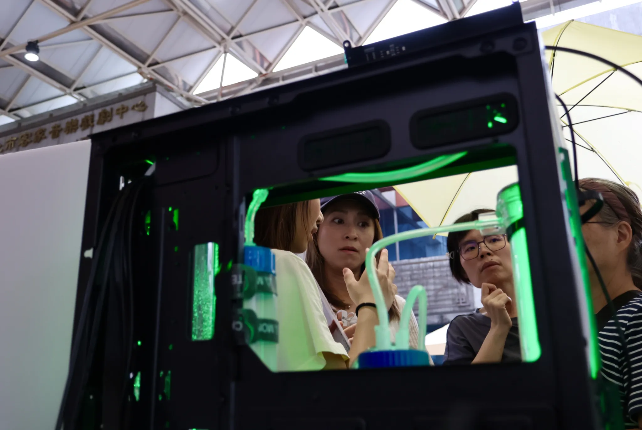 Visitors leaning in to look at the bioreactor prototype glowing green inside its black case.