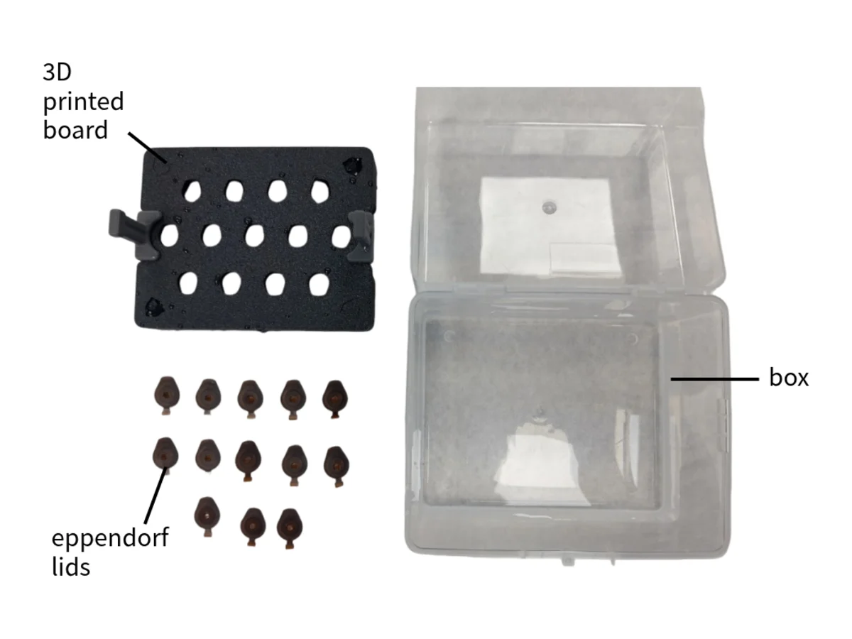 The 3D-printed board with a handle on each side, fifteen Eppendorf lids and the open tip box.