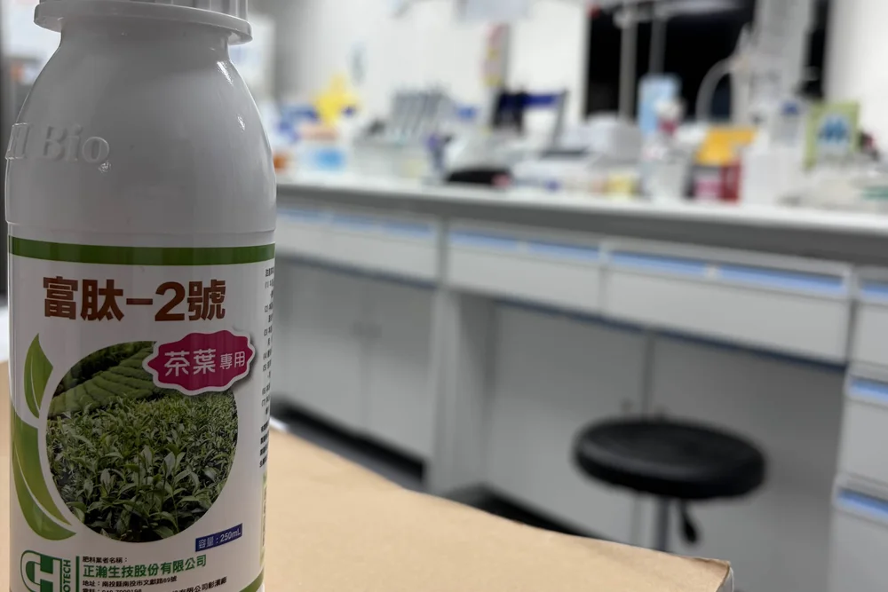 A white bottle labelled 富肽2號 standing on a laboratory bench, the rest of the bench out of focus behind it.