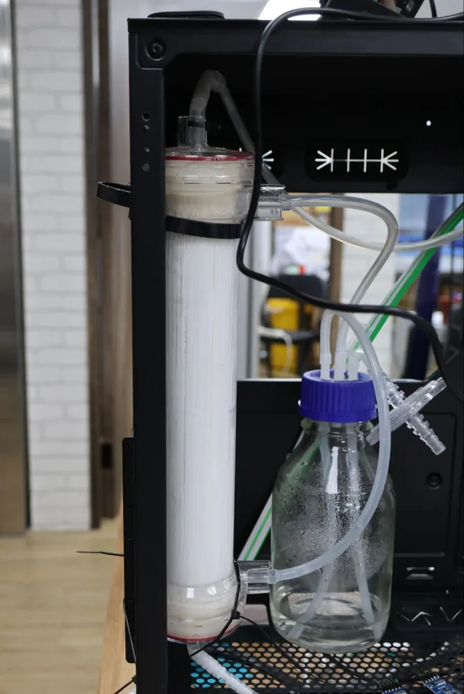 The hollow fibre membrane module standing upright in the bioreactor, connected to tubing and a medium bottle, with a pressure gauge and control panel.