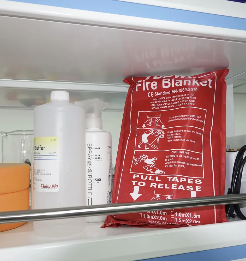 A red fire blanket pouch hanging by a lab shelf that holds buffer solutions and acid bottles.