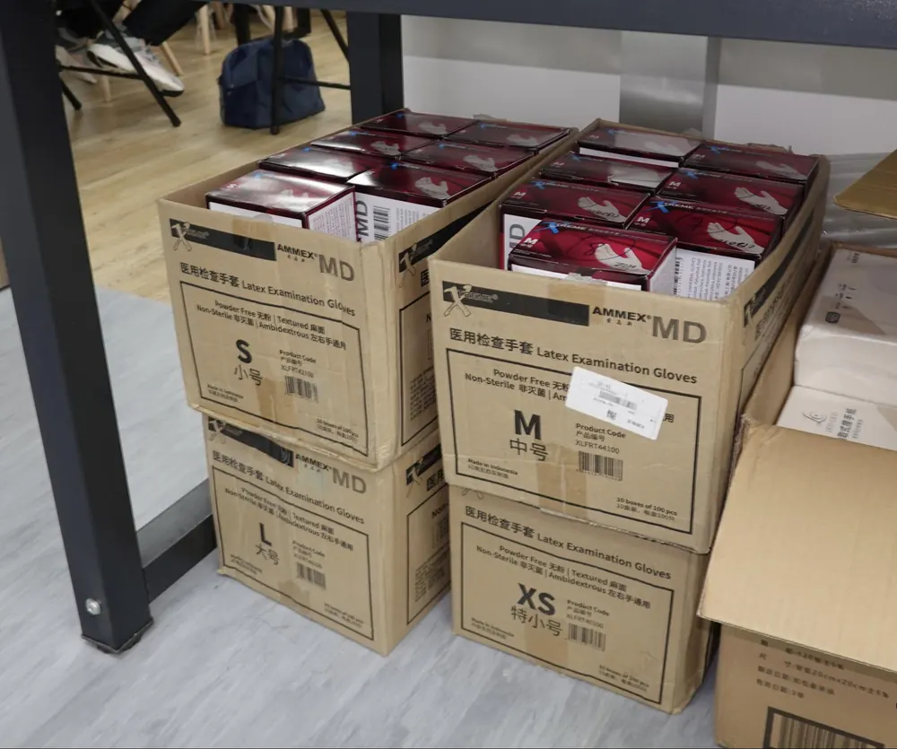 Cartons of examination gloves in sizes XS, S, M and L stacked on the floor.