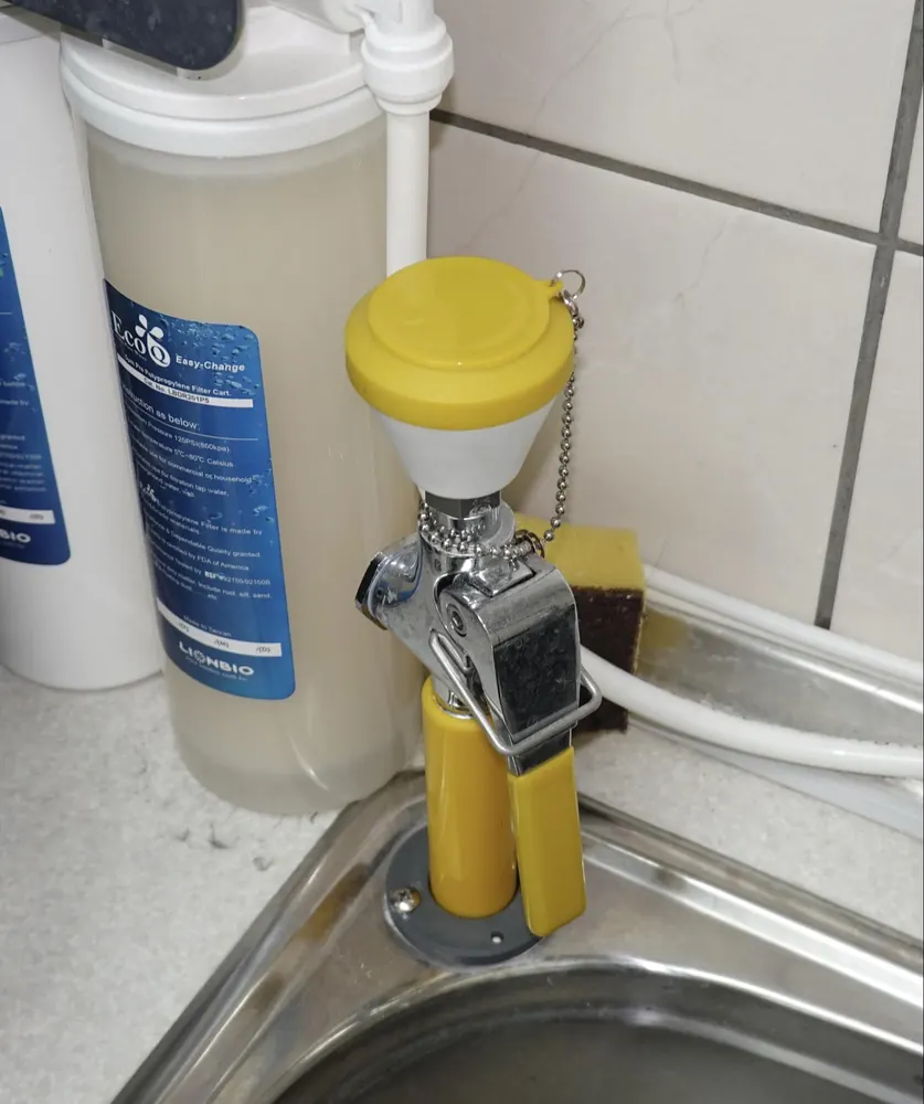 A wall-mounted emergency eyewash station with a yellow pull-down lever above a sink.