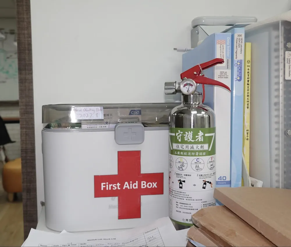 A white first aid box with a red cross, beside a fire extinguisher and reference books.