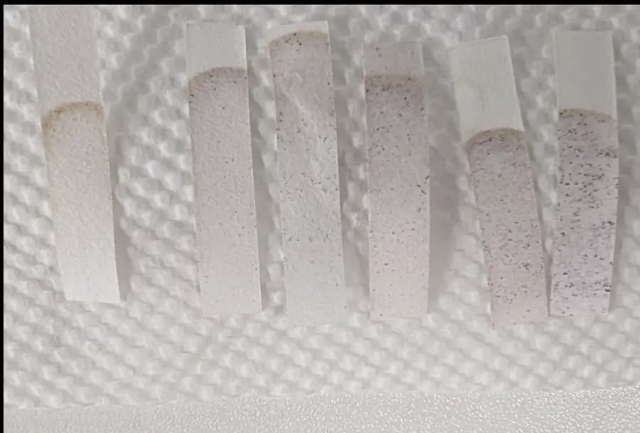 Seven starch-iodide test strips laid side by side on a white cloth, their dark speckling differing from strip to strip