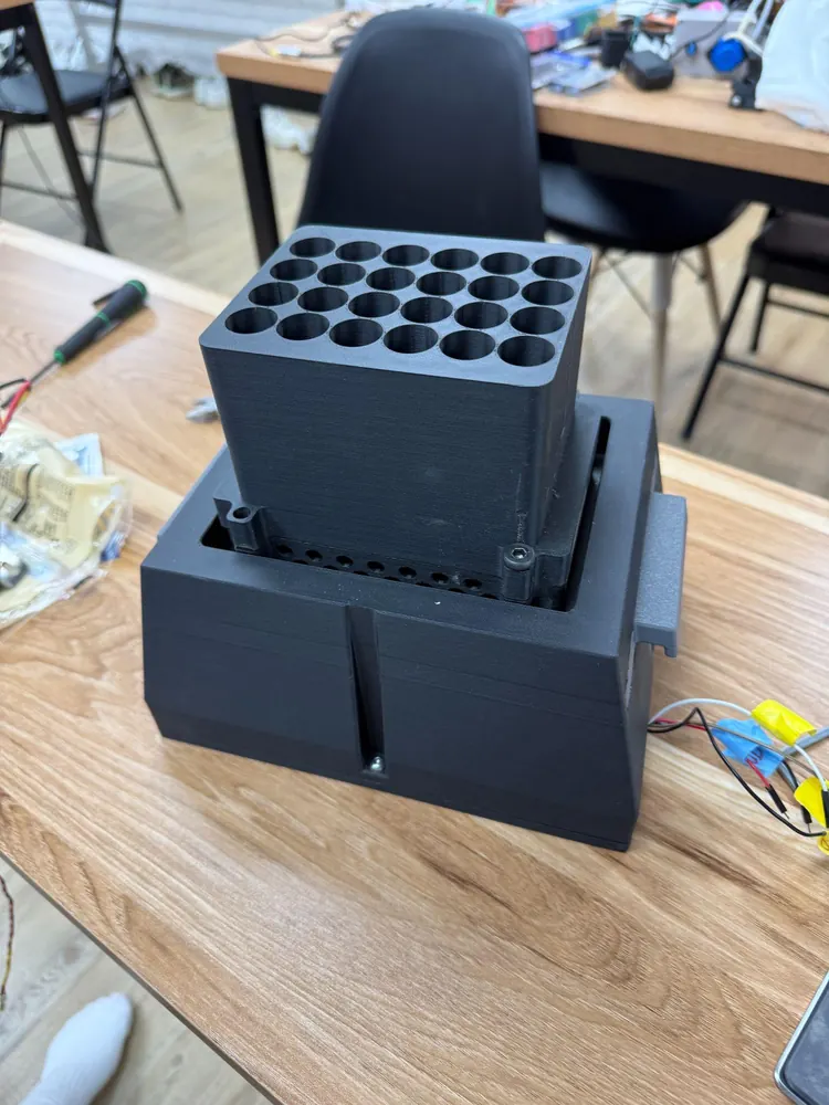 The final LPA on a desk: a black printed tube holder with 24 round bores seated in the top of the black housing, the slider tab on its side.