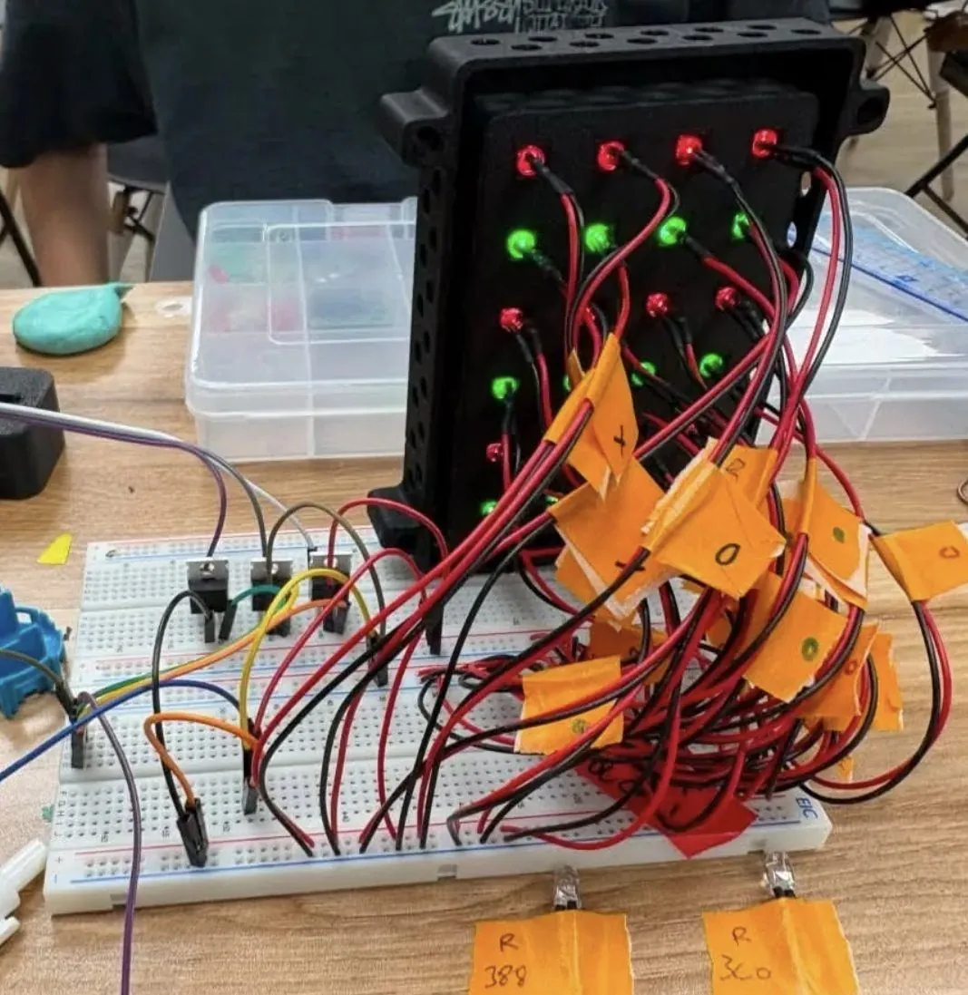 The black LED holder standing upright with green and red LEDs lit, tagged red and black leads running from it to a breadboard in front.