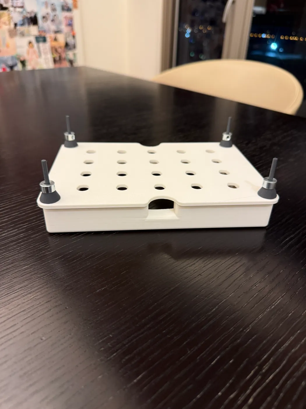The first printed floating plate on a dark table: a white slab perforated with a grid of holes over a closed hollow frame, with a threaded pole and a washer stack rising from each of the four corners.