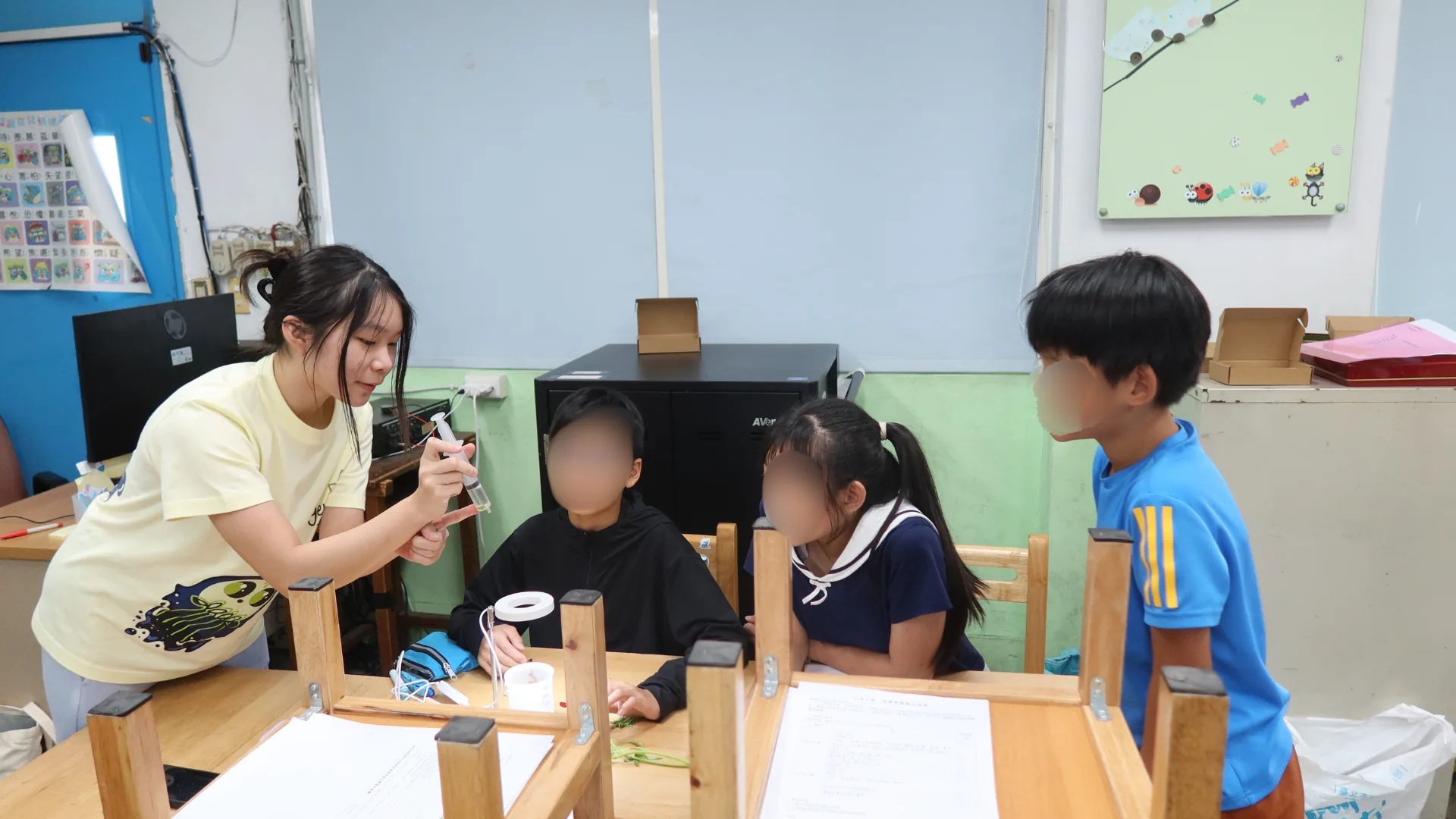 A ReLEAF team member demonstrating the spinach leaf-disk experiment to elementary students seated around a table.