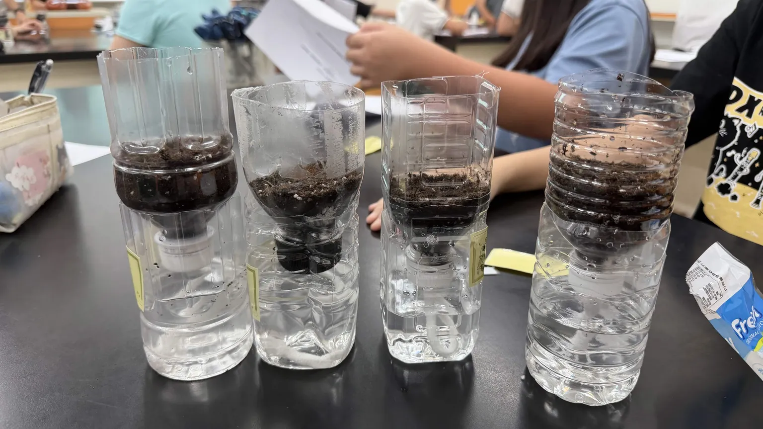 Four finished self-watering planters made from cut PET bottles, soil in the top half and water in the bottom.