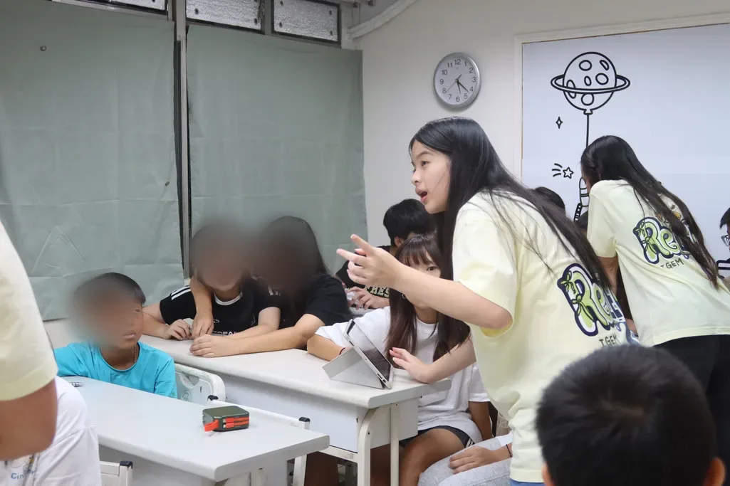 A ReLEAF team member leaning over a desk and pointing, talking with a group of junior high students.