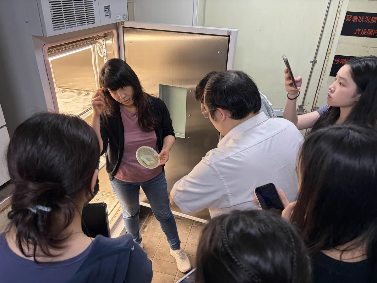Prof. Cheng holding a plate of seedlings in front of an open growth chamber, with students around her.