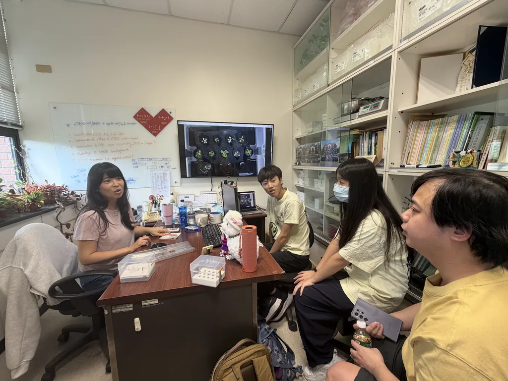 Prof. Cheng at her desk with students seated around her, plant images on the screen behind.
