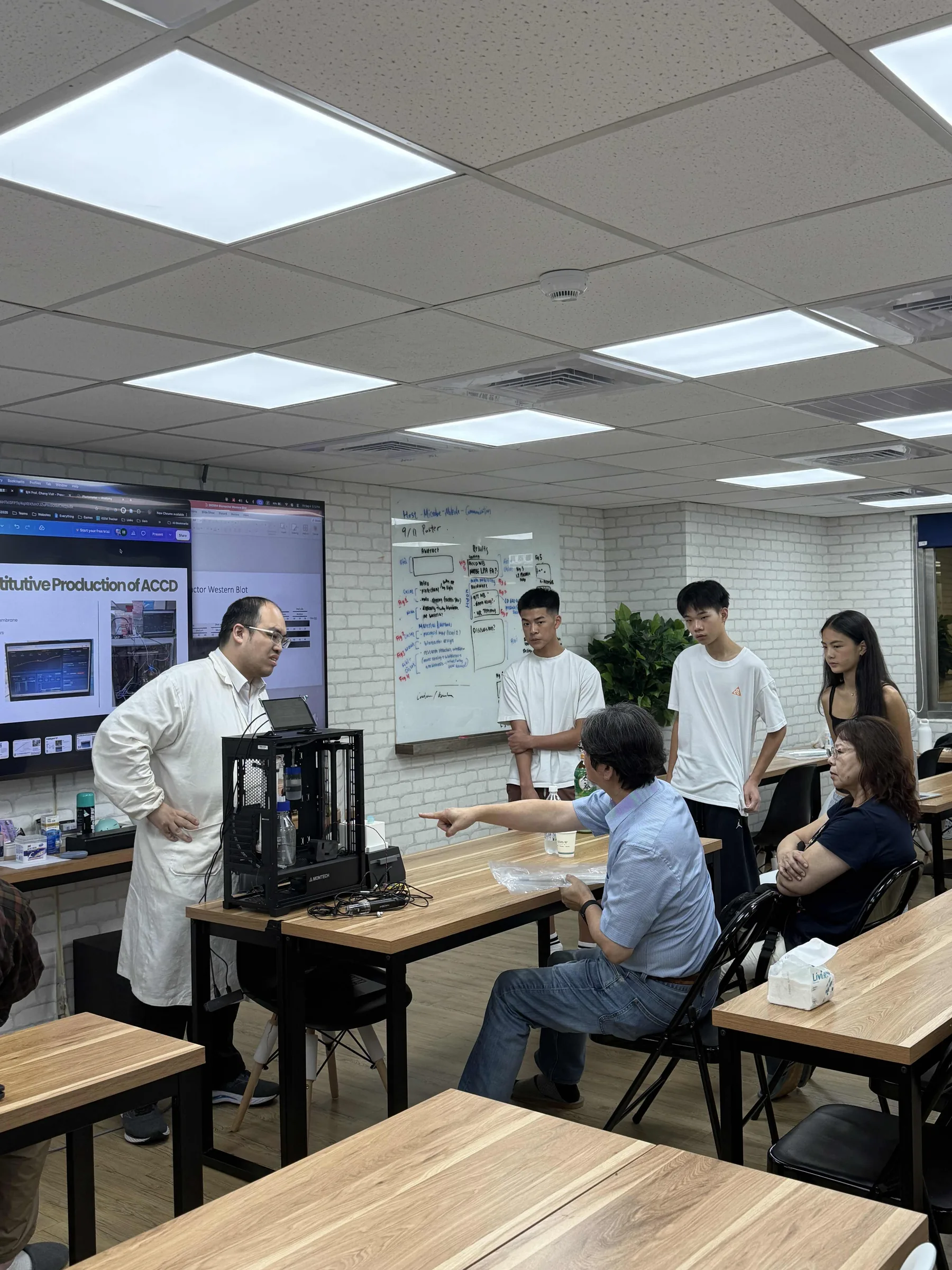 The same room from further back: the bioreactor on the table, Prof. Chang seated and students along the wall.