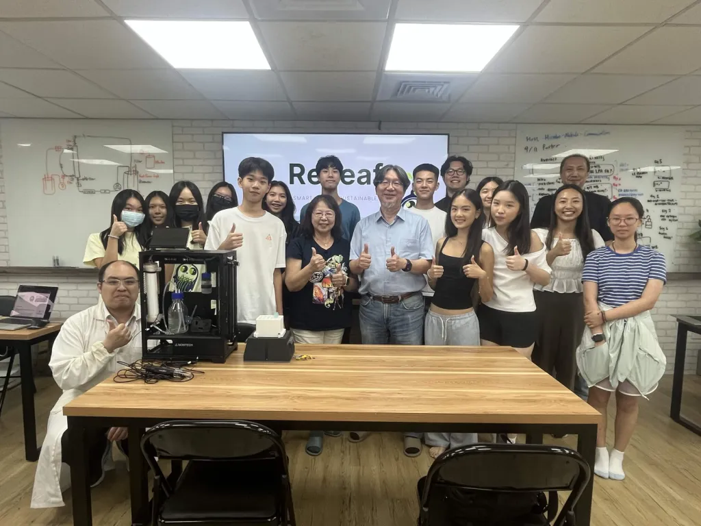 The team with Prof. Chang, thumbs up, behind a table holding the bioreactor.