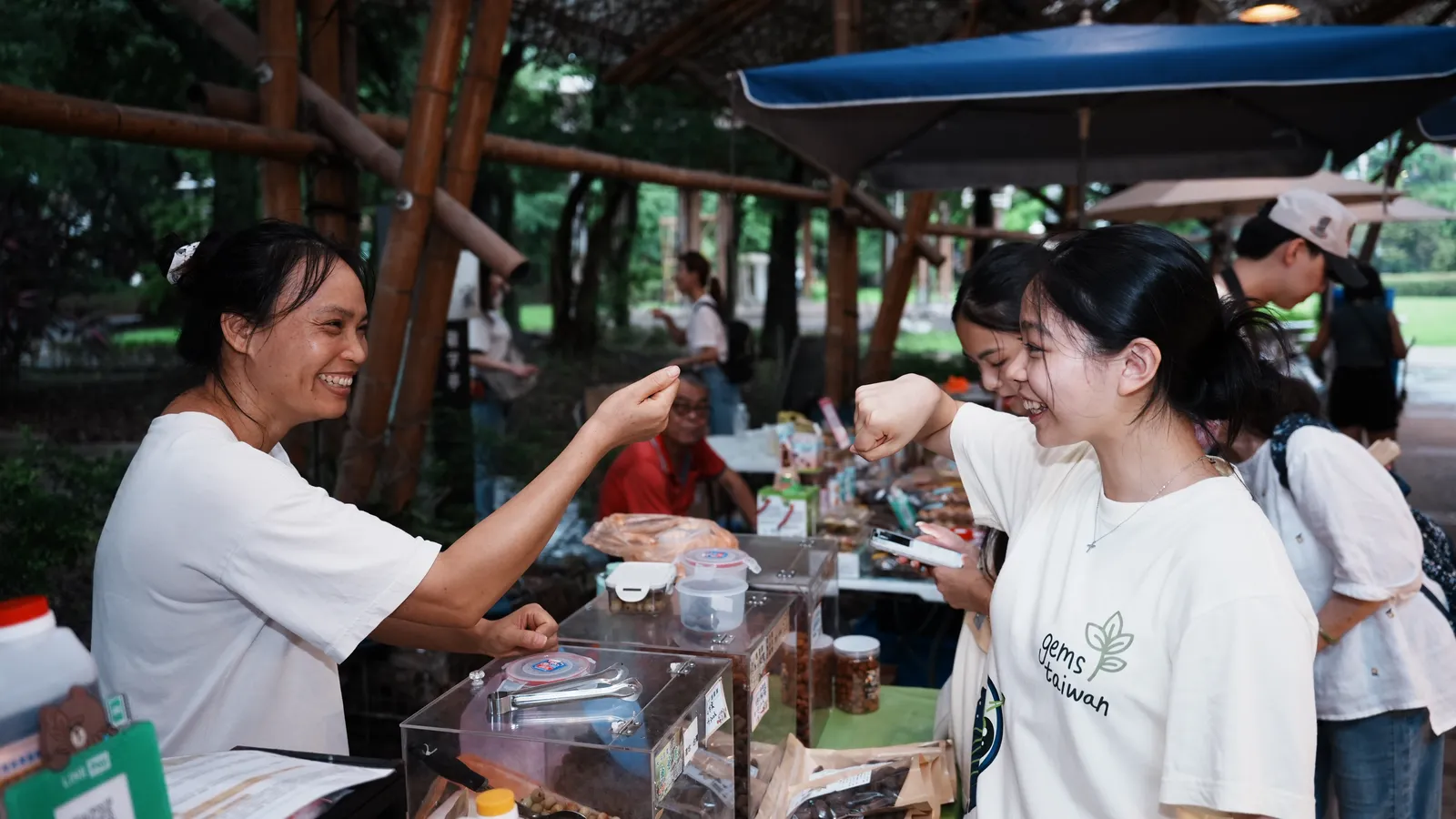 A stallholder showing jars to two smiling students.